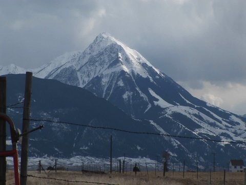 A snow-capped mountain watches over a ranch with barbed-wire fences.