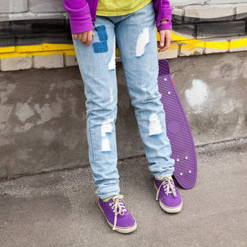 Teenager in jeans and gumshoes with skateboard