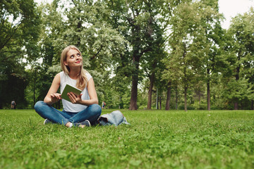 Naklejka na ściany i meble Happy young blonde woman with digital tablet sitting at park.