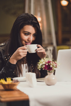 Woman drinking coffee while using her laptop