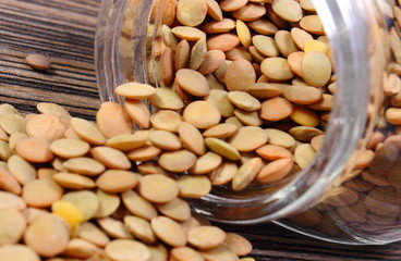 Lentil spilling out of glass jar. Wooden background