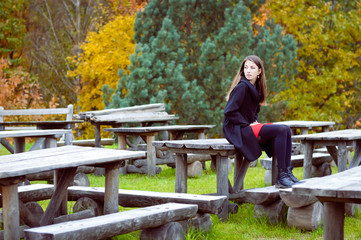 Naklejka na ściany i meble Woman sitting on old park cafe wooden table in autumn