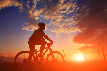 Silhouette of a biker and bicycle on sky background.