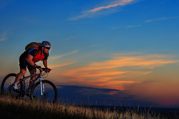 Silhouette of a biker and bicycle on sunset background.