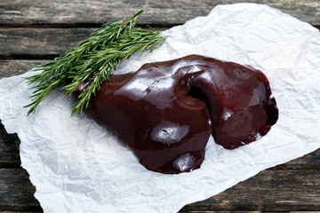 Raw Lamb liver on crumpled paper, decorated with Rosemary. on old  wooden table