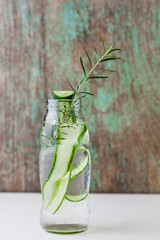 Glass bottle of cucumber and rosemary on wooden table