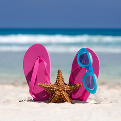 Fototapeta na wymiar Pink flip flops, swimming glasses and starfish on white sandy be
