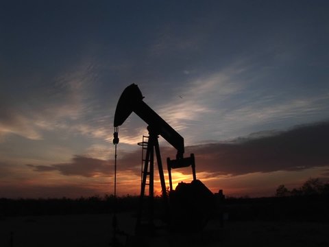 Medium shot of a silhouetted oil pump turning in the New Mexico desert.
