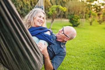 Senior european couple talking lying down and playing in a hammock - Powered by Adobe