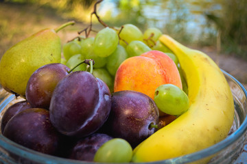 Fresh organic fruits on the plate. Sunny day. River bank