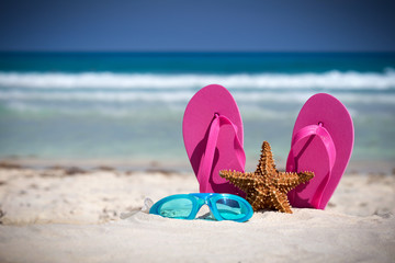 Pink flip flops, swimming glasses and starfish on white sandy be