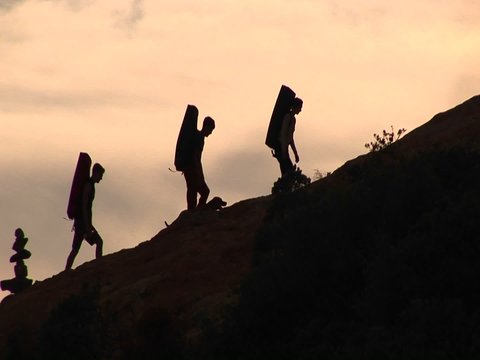 Medium-shot of a group of silhouetted backpackers and a dog climbing a rock structure.