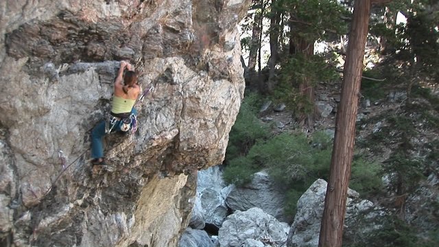Pan-up of a rock climber making her way up a perpendicular rock cliff face.