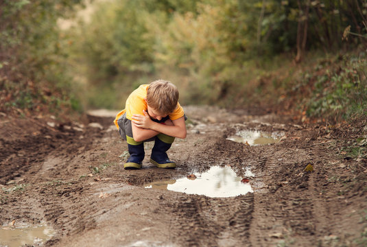 Boy look into the puddle on the country road
