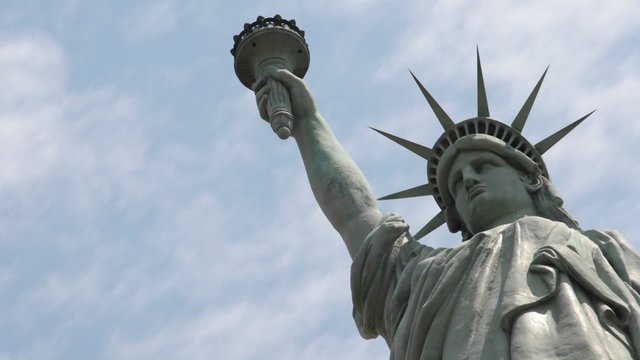 Time lapse of clouds behind the Statue Of Liberty in this shot which says patriotism and patriotic values.