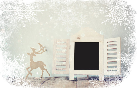 abstract filtered photo of decorative chalkboard frame and wooden deer over wooden table. ready for text or mockup with snowflakes overlay
