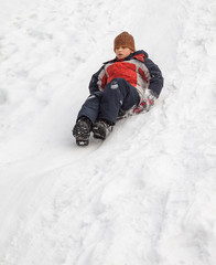 Fototapeta na wymiar Winter fun - sledding at winter time. Young boy enjoying a sledge ride in a snowy winter park.