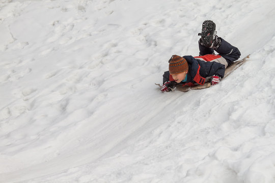 Winter fun - sledding at winter time. Young boy enjoying a sledge ride in a snowy winter park.