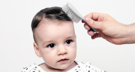 Father hand brushing with a comb his adorable baby hair