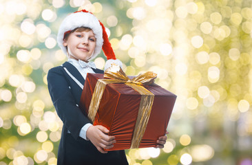 Obraz na płótnie Canvas Beautiful little boy with a big Christmas gift in a Santa Claus hat. Christmas gifts for children. Smart boy Celebrates Christmas. New Year's holidays
