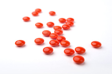 A side view of a heap of red medicine pills on white surface.