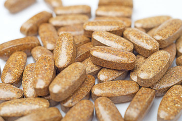 A heap of brown medicine pills on white surface.