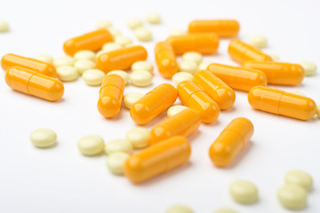 A heap of yellow medicine pills and capsules on white surface.