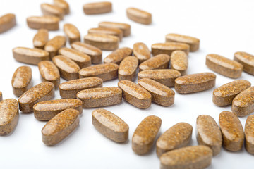 A heap of brown medicine pills on white surface.