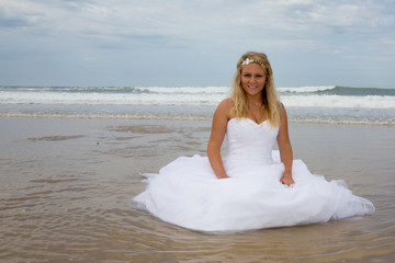 Fototapeta na wymiar A blond woman in her wedding dress at the beach