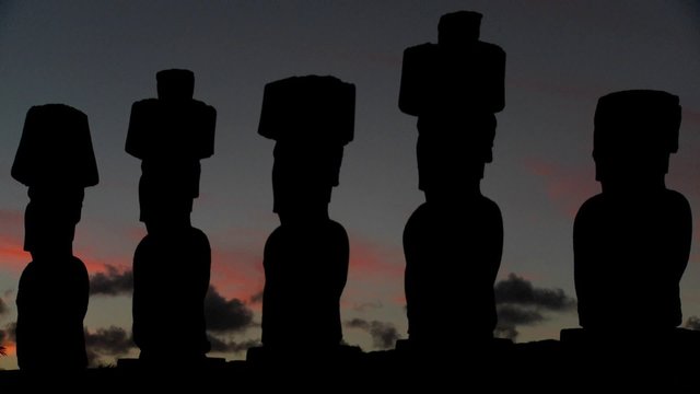 The sun sets behind Easter Island statues.