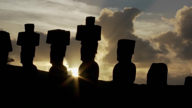 The sun peeks out from behind an Easter Island statue.