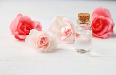 Obraz na płótnie Canvas Pure rose water in glass bottle fresh pink pastel rose blossom delicate, spa beauty care setting, wooden shelf, soft focus