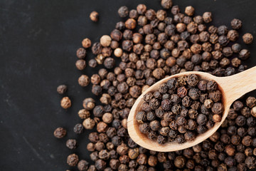 Closeup black pepper whole in wooden spoon on black stone table, top view
