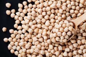 Closeup chickpea in wooden spoon and heap chickpea scattered on the black background, top view