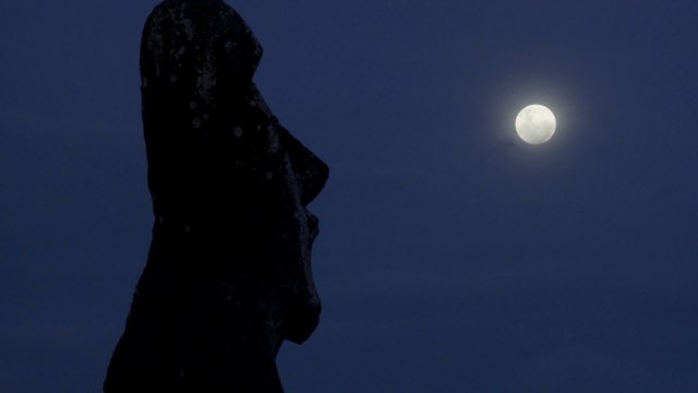 An Easter Island statue is silhouetted in the moonlight.