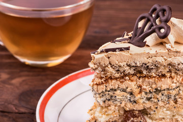 Piece of cake with chocolate and cream on a plate with a cup of herbal tea on a table close-up