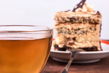 Glass cup of herbal tea and a slice of cake with chocolate and cream on the table