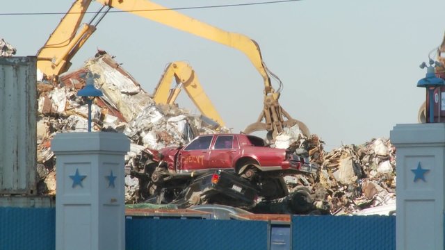 Cranes lift and move scrap metal around abandoned and destroyed cars in a junkyard or scrap metal yard.