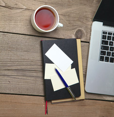 Blank business cards with pen, laptop and tea cup on wooden