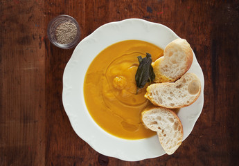 pumpkin soup in a white plate on a wooden background. with sage.