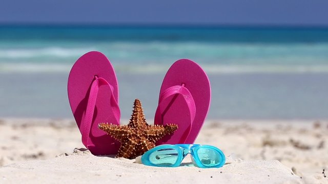 Pink flip flops, swimming glasses and starfish on white sandy beach. Summer vacation concept
