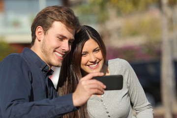 Happy couple watching media in a smart phone outdoors