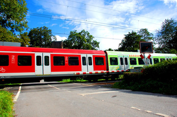 Obraz premium Zug mit verschiedenfarbigen Waggons passiert Bahnübergang 