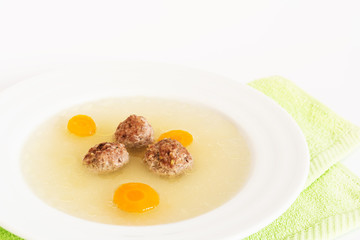 Plate of soup with carrot and meat balls on green towel