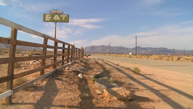 Shadows fall around an abandoned diner with a sign reading eat.