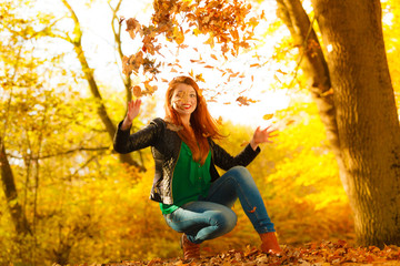 Girl relaxing in autumn park throwing leaves up in the air.