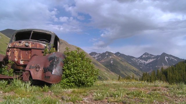 Beautiful time lapse traveling shot across Rocky Mountains with old abandoned car in foreground.