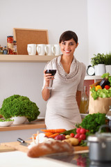 A young woman standing in her kitchen holding a glass of red