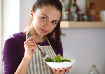 A young woman eating salad in her kitchen .