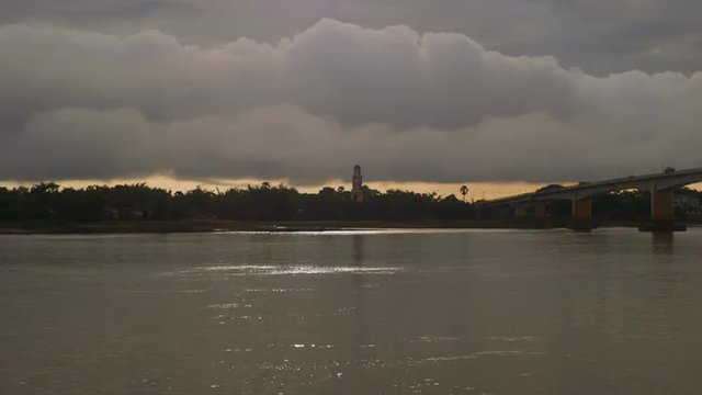 Sparkling light of the sunset on the river and cloudy sky over an old lookout tower by the riverside in the background